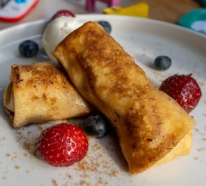 Closeup shot of cheese blintz with strawberries and blueberries on a white plate