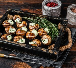 French gourmet - Escargot Snails with garlic butter in a wooden tray. Wooden background. Top view