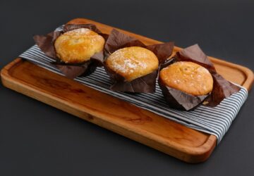 Three muffins wrapped in paper on wooden plate