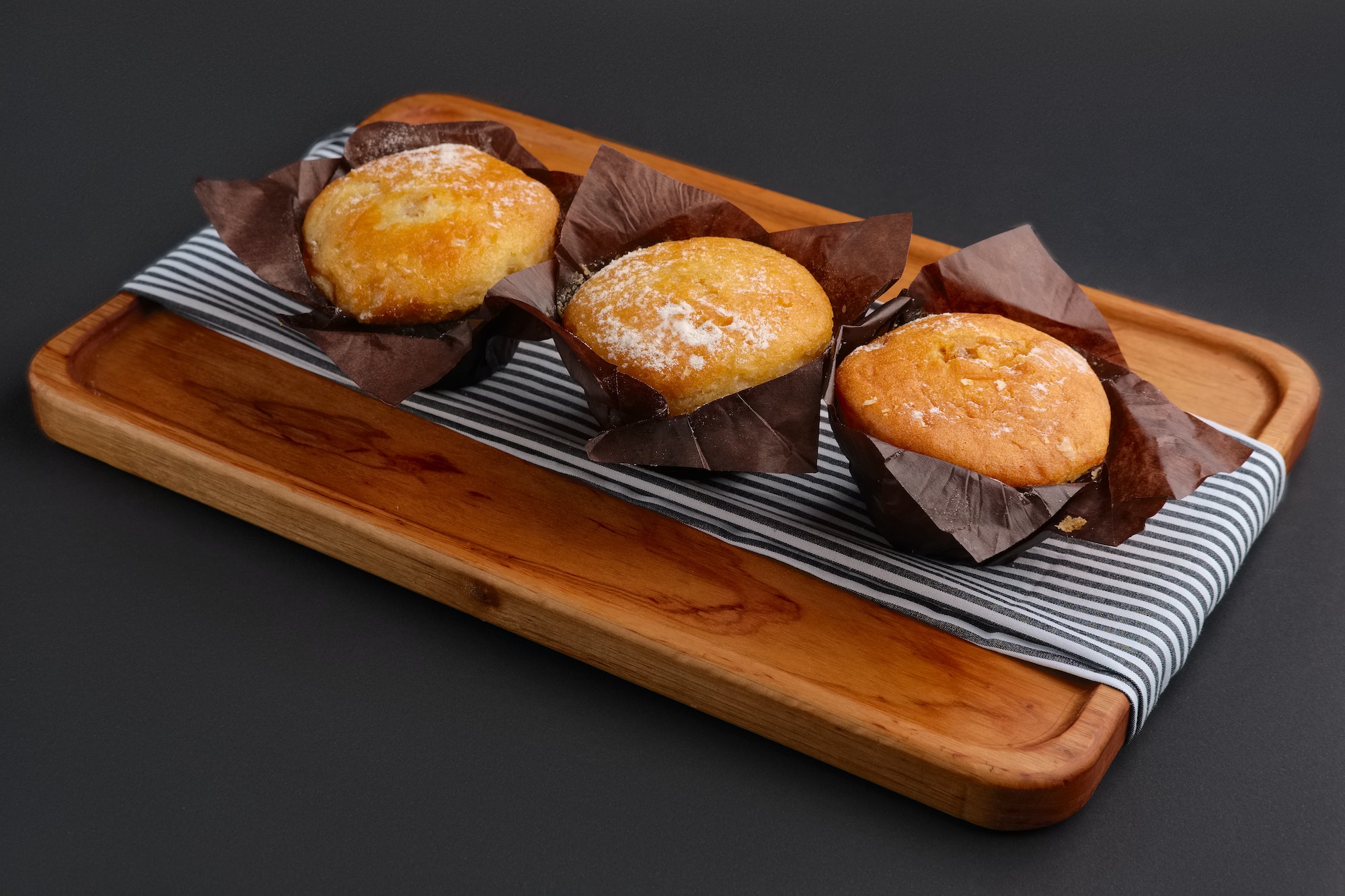 Three muffins wrapped in paper on wooden plate
